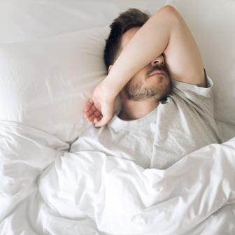 Mann im Bett hält Arm vor Gesicht