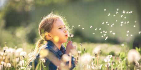 Mädchen in Wiese bläst Pusteblume